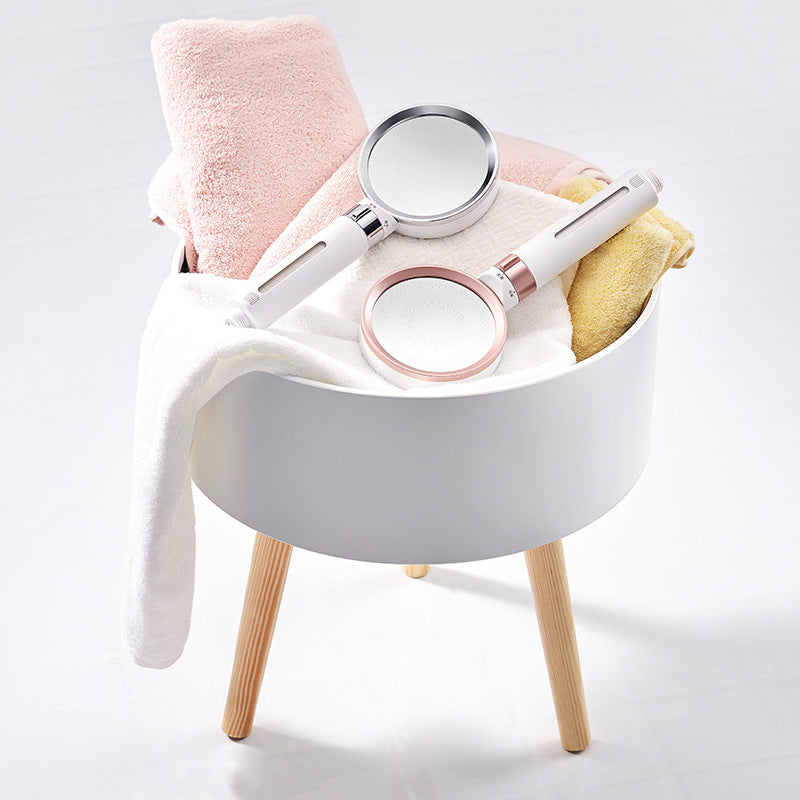 White stool with a pink towel, white handheld showerhead, and round mirror.